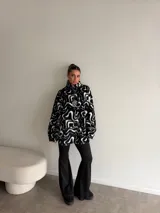 Buzo de peluche con estampado animal print, cuello alto con cierre frontal parcial y detalle de etiqueta decorativa en el pecho.