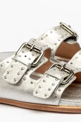 Sandalias de cuero color negro con dos tiras anchas sobre el empeine, cada una con hebillas metálicas ajustables y detalles de tachas plateadas. La suela es de cuero con un borde de color madera.