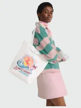 Bolso tote mediano de lona color blanco con diseño estampado frontal que incluye un caballo, olas, un sol y palmeras, junto al logo de la marca. Presenta detalles en cuero blanco en la solapa superior y asas largas para llevar al hombro.