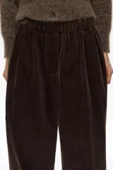 Pantalón de corte recto y holgado confeccionado en pana de algodón color marrón oscuro. Presenta tiro medio, cintura elástica y bolsillos laterales.