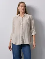 Camisa blanca de lino con cuello con solapa, manga larga regulable con presilla y botón, y abertura central con botones.
