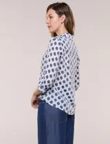 Camisa de gasa blanca con estampado de lunares en tonos azules, cuello con solapa, cierre frontal de botones, bolsillo aplicado en el pecho y detalle de nudo en el dobladillo inferior. Cuenta con mangas largas regulables.