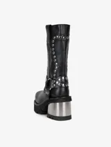 Bota negra de cuero hasta media pantorrilla, con plataforma y taco metálico plateado. Presenta detalles de tachas plateadas y correa con hebilla metálica.