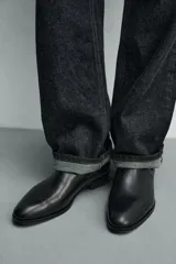 Bota estilo chelsea de cuero color marrón, con paneles elásticos laterales, tirador trasero y horma en punta con suela de tacón bajo.