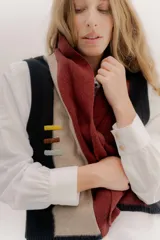 Chaleco abierto de tejido de punto, con diseño de bloques de color verticales en gris claro, negro y gris oscuro. Presenta un cuello ancho tipo chal y un detalle de tres pequeñas aplicaciones bordadas horizontales en tonos verde oliva, naranja quemado y celeste pálido en el frente.