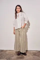 Blusa de algodón peinado color off-white, con cuello mao, cierre frontal de botones, mangas tres cuartos abullonadas con puños con volados, detalles de alforzas y apliques de encaje en el frente y los hombros.