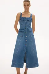 Vestido midi de denim de algodón con breteles anchos, escote cuadrado, botonadura frontal y múltiples bolsillos con solapa. Presenta un cuerpo entallado y falda acampanada con costuras visibles.