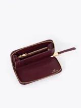 Maxi billetera de cuero vacuno con diseño matelassé en forma de V. Presenta un aplique metálico dorado en forma de labios en el frente y cierre perimetral con tirador de cuero.