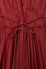 Vestido midi color rojo oscuro (terracota/vino) con escote pico pronunciado, manga corta tipo mariposa y detalle de pinzas en el busto. Presenta un cinturón fino tipo cordón ajustable a la cintura y cierre frontal con botones ocultos.