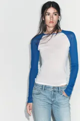 Camiseta de manga larga con cuerpo blanco y mangas raglán azules. Tiene cuello redondo y corte slim fit.