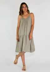 Vestido solero corto color beige, con tirantes finos, escote en V con frunces en el busto y corte con volado en la parte inferior.