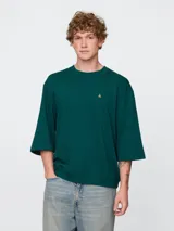 Remera de corte oversized color verde oscuro, con cuello redondo y mangas de largo medio. Presenta un pequeño bordado del oso Brannan en el pecho.