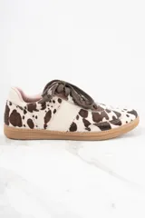 Zapatillas bajas con estampado de vaca en tonos marrón y blanco, con cordones marrones y suela de goma color caramelo.