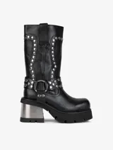 Bota negra de cuero hasta media pantorrilla, con plataforma y taco metálico plateado. Presenta detalles de tachas plateadas y correa con hebilla metálica.