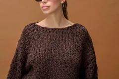 Sweater de tejido de punto grueso con textura trenzada y destellos de lurex, en color chocolate. Presenta un diseño oversize con cuello redondo amplio y mangas largas con puños ajustados.