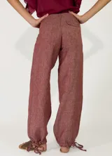 Pantalón de lino color beige, de corte holgado tipo jogger con puños ajustables con cintas en los tobillos, bolsillos laterales y cierre frontal con botón y cremallera.