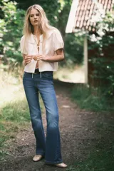 Blusa de viscosa con acabado satinado, cuello Peter Pan fruncido con detalle de encaje, frente abierto con cierre de triple tira y mangas cortas abullonadas con puños elásticos.