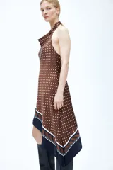 Vestido corto asimétrico de satén color marrón con lunares blancos, escote drapeado tipo halter y espalda descubierta. Cuenta con una franja ancha negra y rayas en la parte inferior.