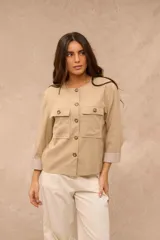 Campera ligera color beige, de cuello redondo y manga larga con puños vueltos de tela a rayas. Cuenta con cierre frontal de botones y dos bolsillos con solapa en el pecho.