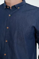 Camisa de jean azul oscuro de manga larga con cuello abotonado y bolsillo en el pecho.