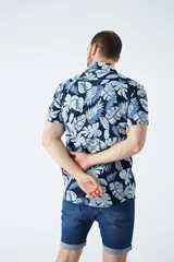 Camisa de manga corta con estampado botánico de hojas en tonos azul y blanco. Presenta cuello clásico, cierre frontal abotonado y corte slim.