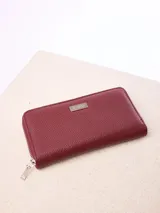 Billetera Rusty modelo Novadi W26, de color bordó con textura granulada, cierre perimetral de cremallera y placa metálica con la marca grabada en el frente.