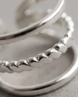 Set de tres anillos de acero quirúrgico en color plateado, con diseños minimalistas que incluyen dos bandas lisas y una con textura facetada o entrelazada.
