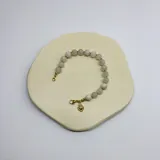 Pulsera de cuentas de piedra de luna de 8 mm, con separadores de nudos de hilo beige y piezas metálicas con baño de oro. Incluye un dije colgante en forma de corazón con diseño de corazón sagrado.