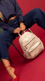 Mochila color marrón claro de símil cuero con bolsillos frontales con cierre. Tiene asa de mano rígida y correas regulables.