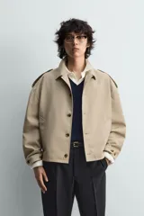 Cazadora color beige, estilo cropped, con cuello de solapa, manga larga con puños ajustables y trabillas en los hombros. Presenta bolsillos de vivo en la cadera y cierre frontal de botonadura.