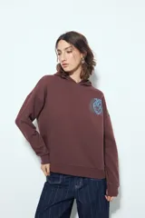 Buzo canguro color marrón con capucha y estampado de un corazón anatómico en azul en el pecho. De silueta relajada y calce cómodo.