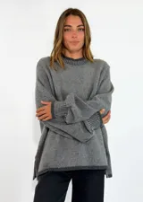 Sweater de punto gris con diseño holgado, cuello redondo, mangas largas con puños acanalados y aberturas laterales en el ruedo.