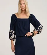 Blusa corta azul marino con escote recto estilo hombro a hombro, mangas largas abullonadas con detalle de bordado decorativo en cuerda clara.