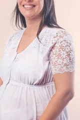 Camisón maternal blanco de algodón elastizado, con escote redondo, mangas cortas de puntilla y detalle de puntilla en los hombros. Presenta cierre frontal con botones y elástico bajo el busto para mayor sujeción.