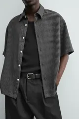 Camisa de corte relajado con textura de rayas verticales, cuello solapa y manga corta. Presenta cierre frontal con botones a tono.