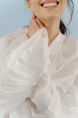 Blusa de algodón color blanco, con cuello alto y lazo frontal para atar. Presenta mangas largas con volados en los puños y un diseño holgado y romántico.