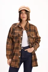 Camisa de corte oversize con estampado de cuadros en tonos marrones y negros. Presenta cuello clásico, cierre frontal de botones metálicos y dos bolsillos con solapa en el pecho.