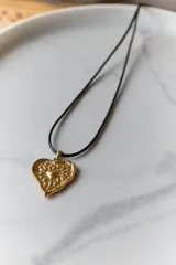 Collar con dije de corazón en acero quirúrgico, con textura irregular y relieve, montado sobre un tiento encerado negro.