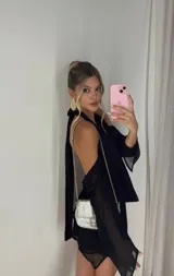 Vestido corto negro con escote halter, hombros descubiertos y mangas largas acampanadas.