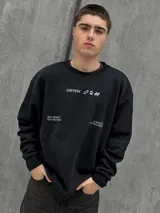 Buzo negro de corte holgado con cuello redondo y puños acanalados. Estampado frontal con la palabra "OSTEN" y la frase "NOT WHERE YOU'RE FROM A MINDSET OF BECOMING" en color blanco.
