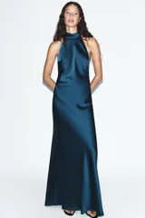 Vestido largo de satén verde oscuro con cuello halter y lazada en el mismo tejido en la parte posterior, diseño sin mangas y espalda descubierta.