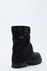 Bota de caña media color negro, con suela robusta dentada y detalle de hebilla ajustable en la parte superior. Presenta una argolla metálica lateral y un diseño de estética urbana con acabado texturizado.