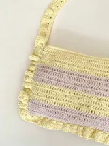 Cartera tipo shoulder bag tejida a crochet en hilo de algodón, con diseño a rayas en tonos de rojo y rosado, y detalles de volados en los bordes y la manija de hombro.