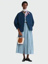 Bolso de mano pequeño con diseño estructurado, confeccionado en lona color beige con bolsillo frontal redondeado en cuero color marrón. Cuenta con asas cortas superiores y herrajes metálicos.