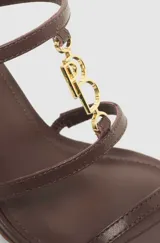 Sandalias de tacón cuña color marrón, con tiras finas en el empeine unidas por un detalle metálico dorado y cierre con hebilla en el tobillo.