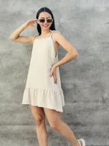 Vestido corto color beige con textura plumetie, breteles finos con lazo y falda con volados.