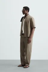 Pantalón de calce relajado confeccionado en tejido de viscosa y yute color tostado. Presenta cintura elástica ajustable con cordón, bolsillos laterales, bolsillos traseros de vivo y cierre frontal con cremallera y botón.