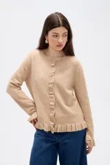 Saco de punto color gris, con cuello redondo, cierre frontal con botones y detalle de volados en la tapeta y el ruedo. Presenta mangas largas con puños acampanados.
