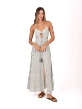 Vestido largo con estampado geométrico en tonos gris y blanco. Presenta un diseño con aberturas laterales en la cintura, escote en V con detalle de abertura circular y tirantes finos. La falda cuenta con una abertura frontal central y un cordón decorativo con borla en la cintura.