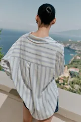 Blusa de manga larga confeccionada en mezcla de viscosa, lino y liocel, con diseño de rayas verticales en tonos celestes y marrones sobre fondo blanco. Presenta cuello solapa con escote en V cruzado.